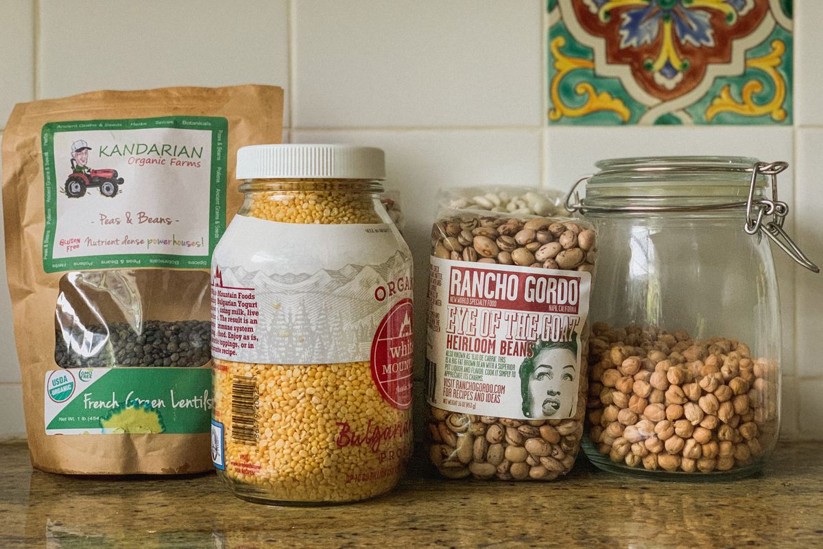 A row of dried beans in bags and jars are arrayed on a counter