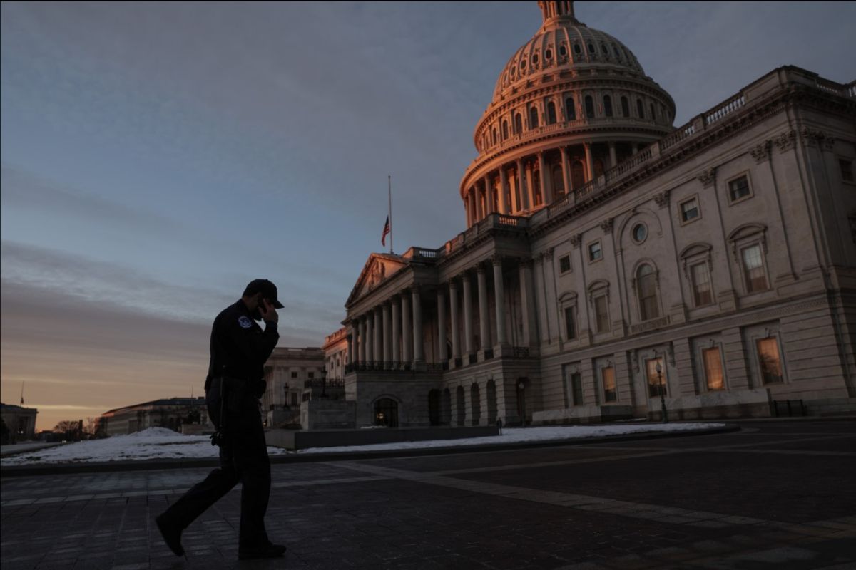 A stooped uniformed police officer walks in front of the east side of the Capitol amid the purple twilight sky.