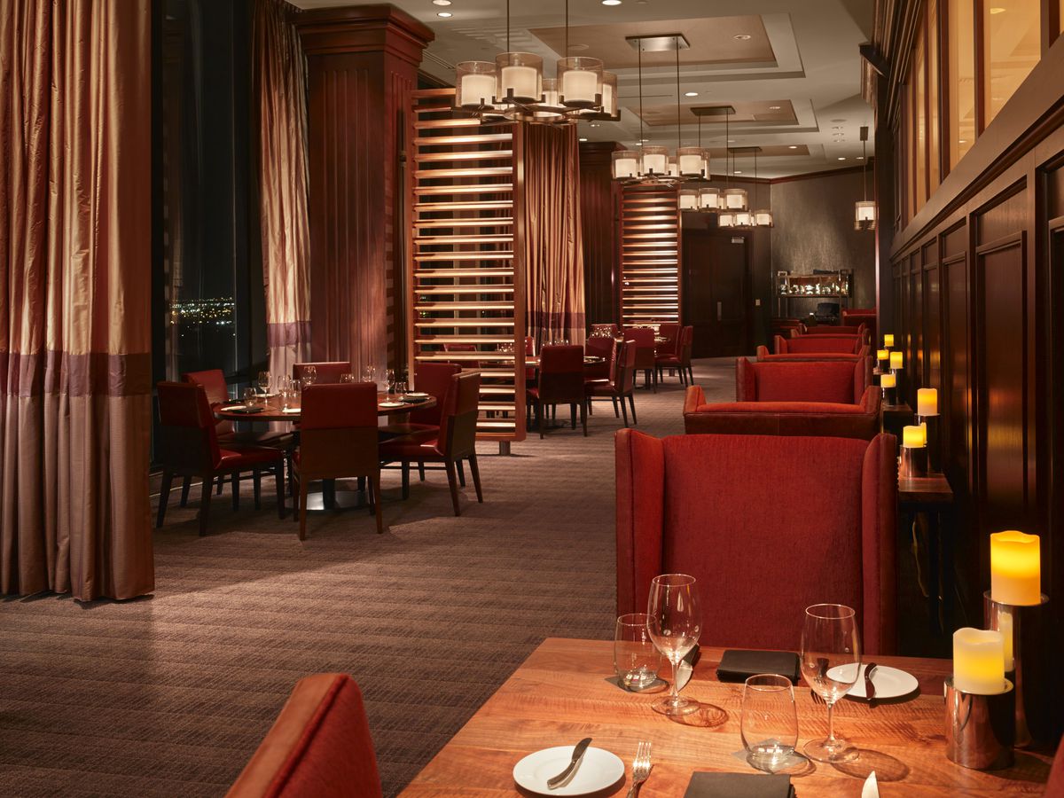 One of the dining areas in SĒR Steak + Spirits at the Hilton Anatole, with burnt orange seating and dark wood tables.