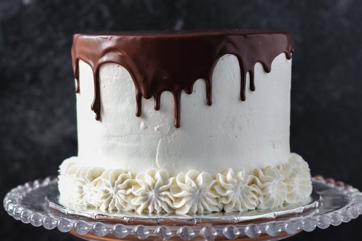 A white cake with chocolate frosting dripping along the sides.
