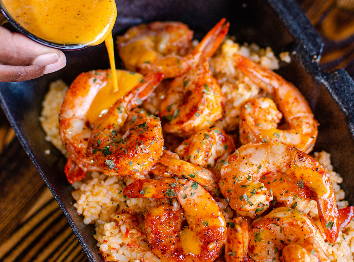 A person pours “crack sauce” on Lotus Seafood’s seasoned shrimp over rice.