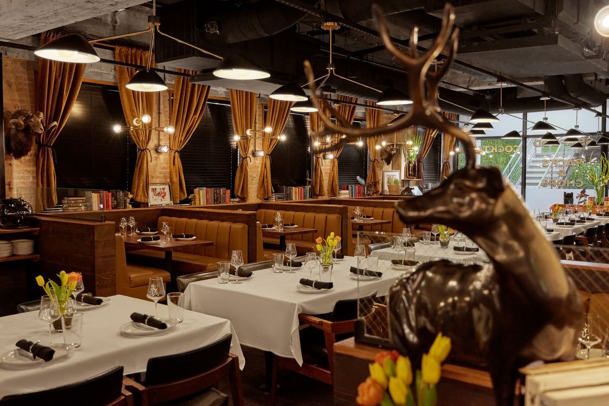 A steakhouse dining room features white cloth covered tables, gold curtains, soft lighting, an in the foreground, a brass ram.