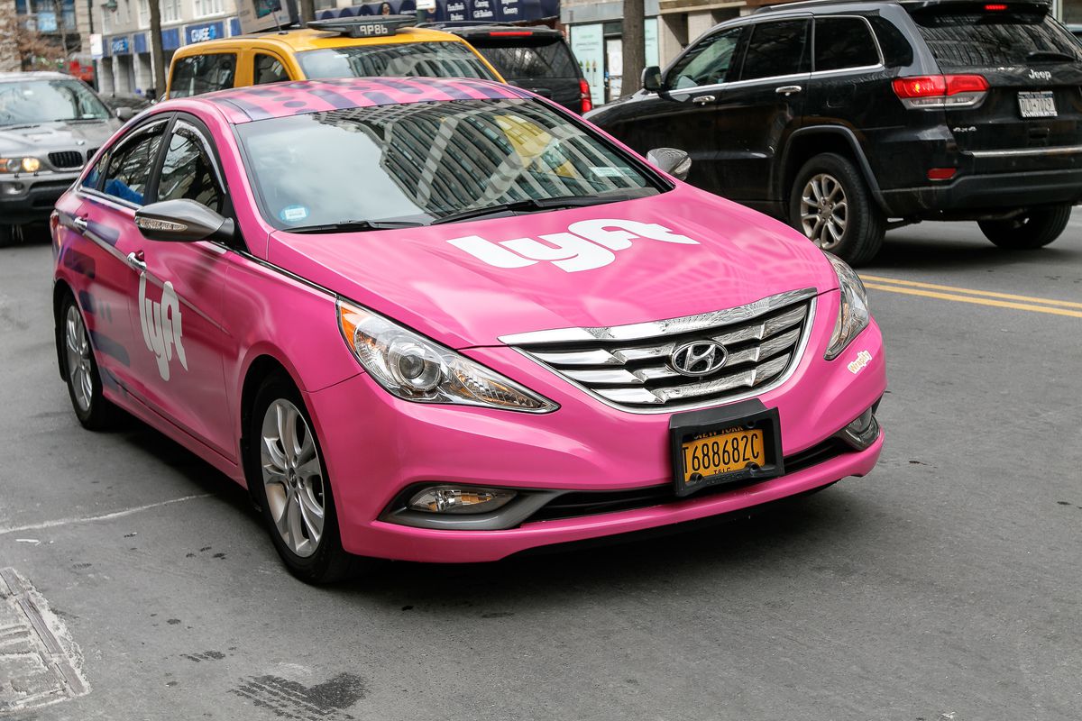 A car painted pink and covered with the Lyft logo driving in New York City.