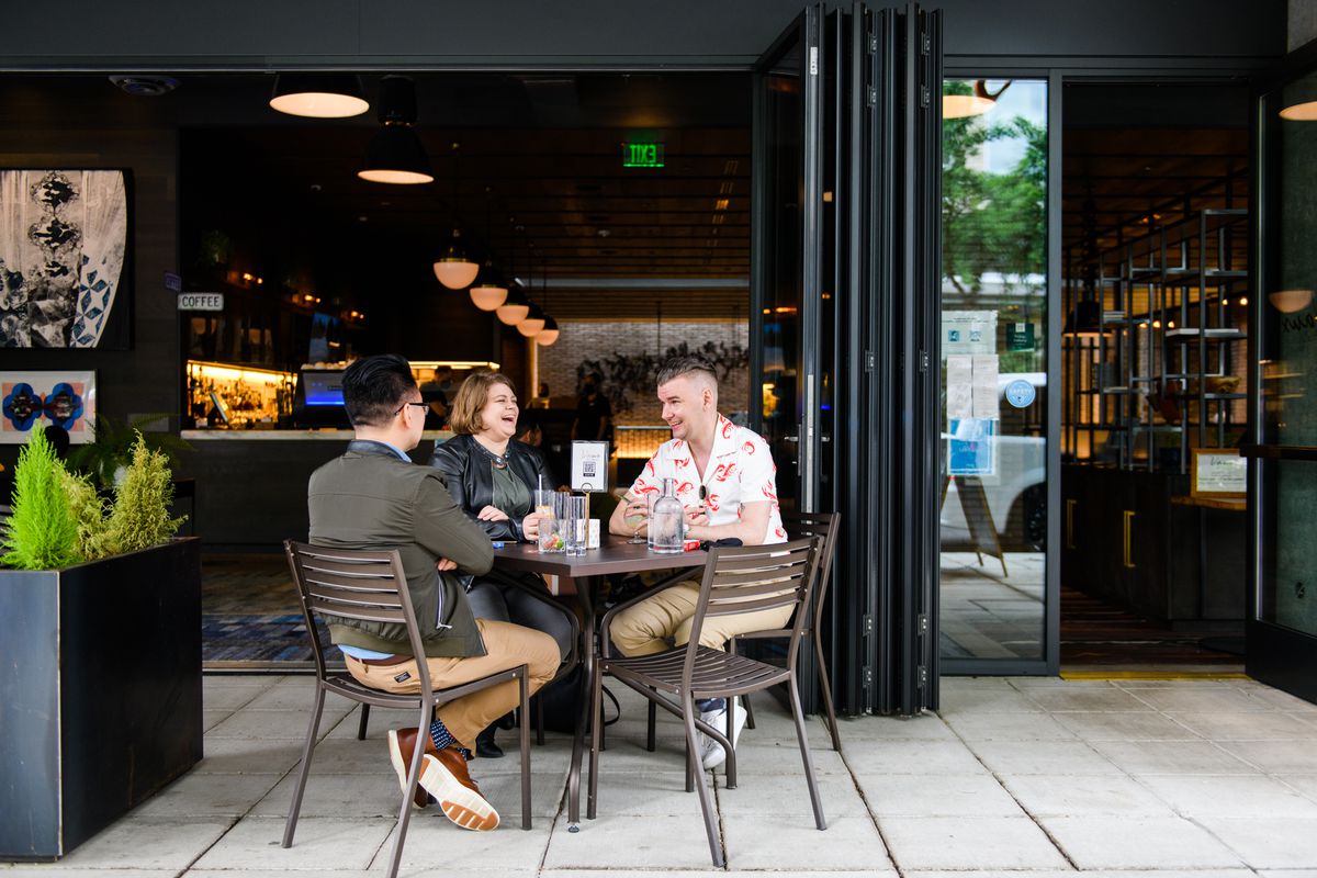 Three diners sit around a table on the patio of Vaux on Sunday, June 21, 2020. A large, garage-door-style window is open into the restaurant.