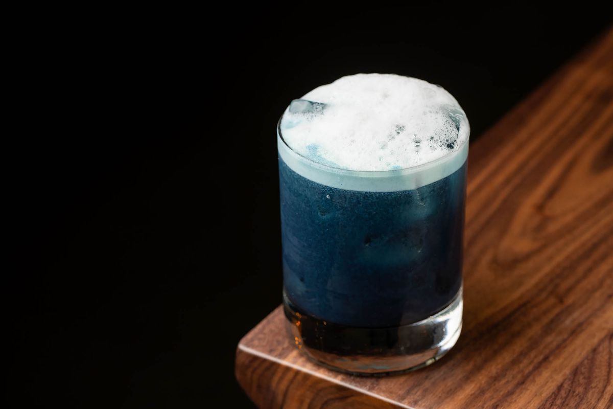 A foamy dark blue drink on the corner of a wooden table at new restaurant Joyce.