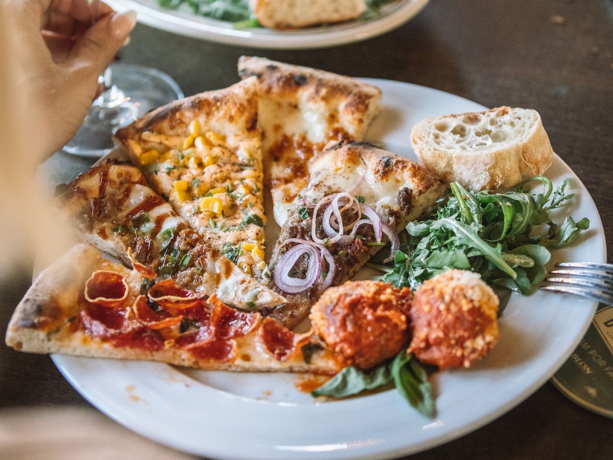 A plate of four varied pizza slices, meatballs, and a green salad.