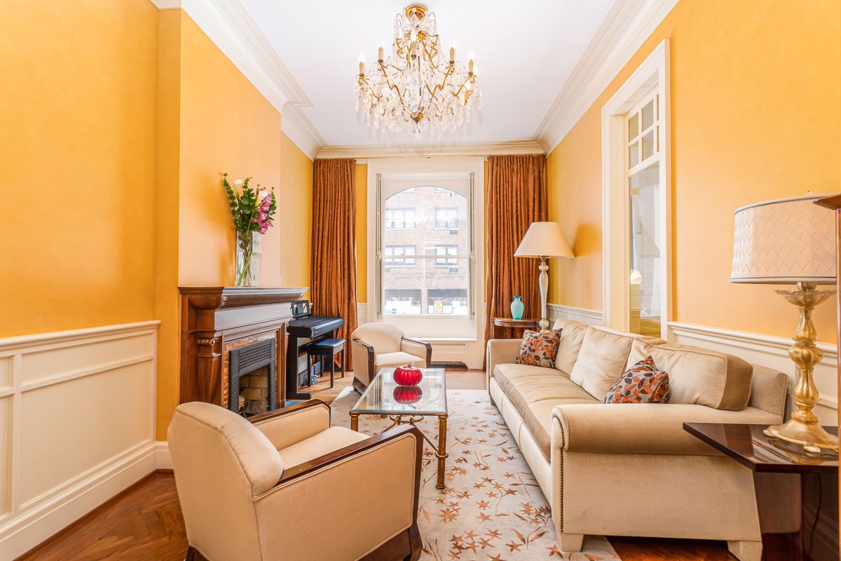 A living area with three couches, a glass coffee table, a fireplace, a chandelier, and yellow walls.