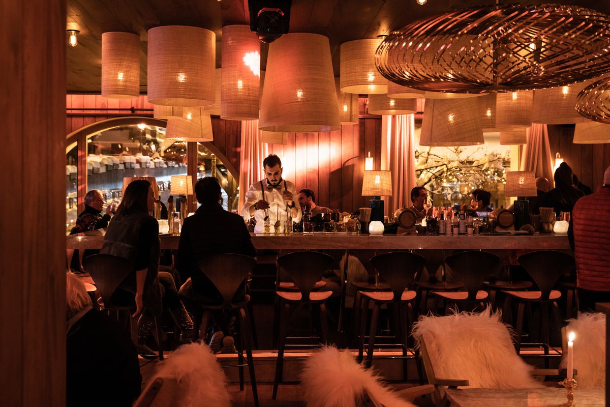 一个黑暗的酒吧内部，一个调酒师在酒吧后面工作，顾客在酒吧的凳子，从各种高设计的灯柔和的照明