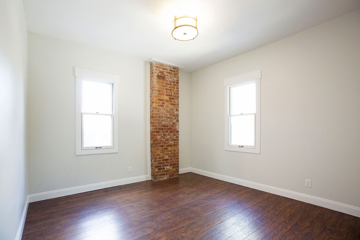 A square, empty room with hardwood floors and white walls.