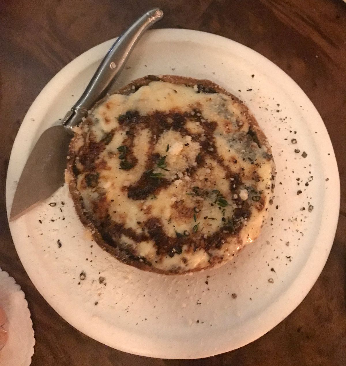 An onion tart sprinkled with pecorino cheese on a white plate with a serving device next to it.
