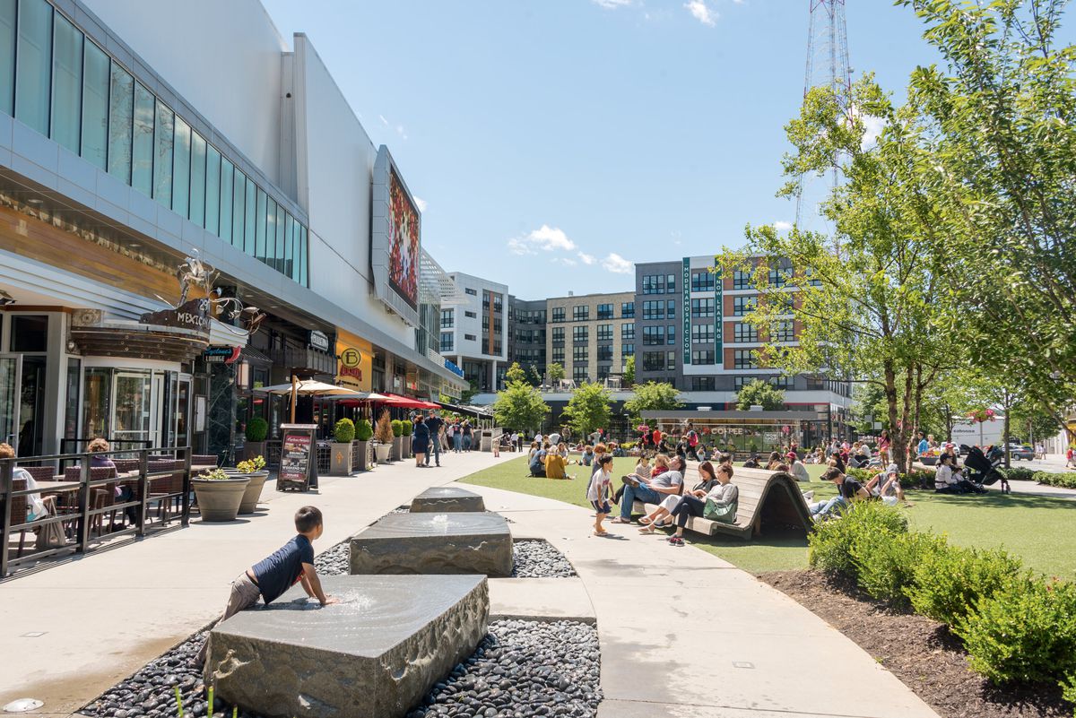 View of a public park in Fairfax County, with storefronts and people sitting on benches.