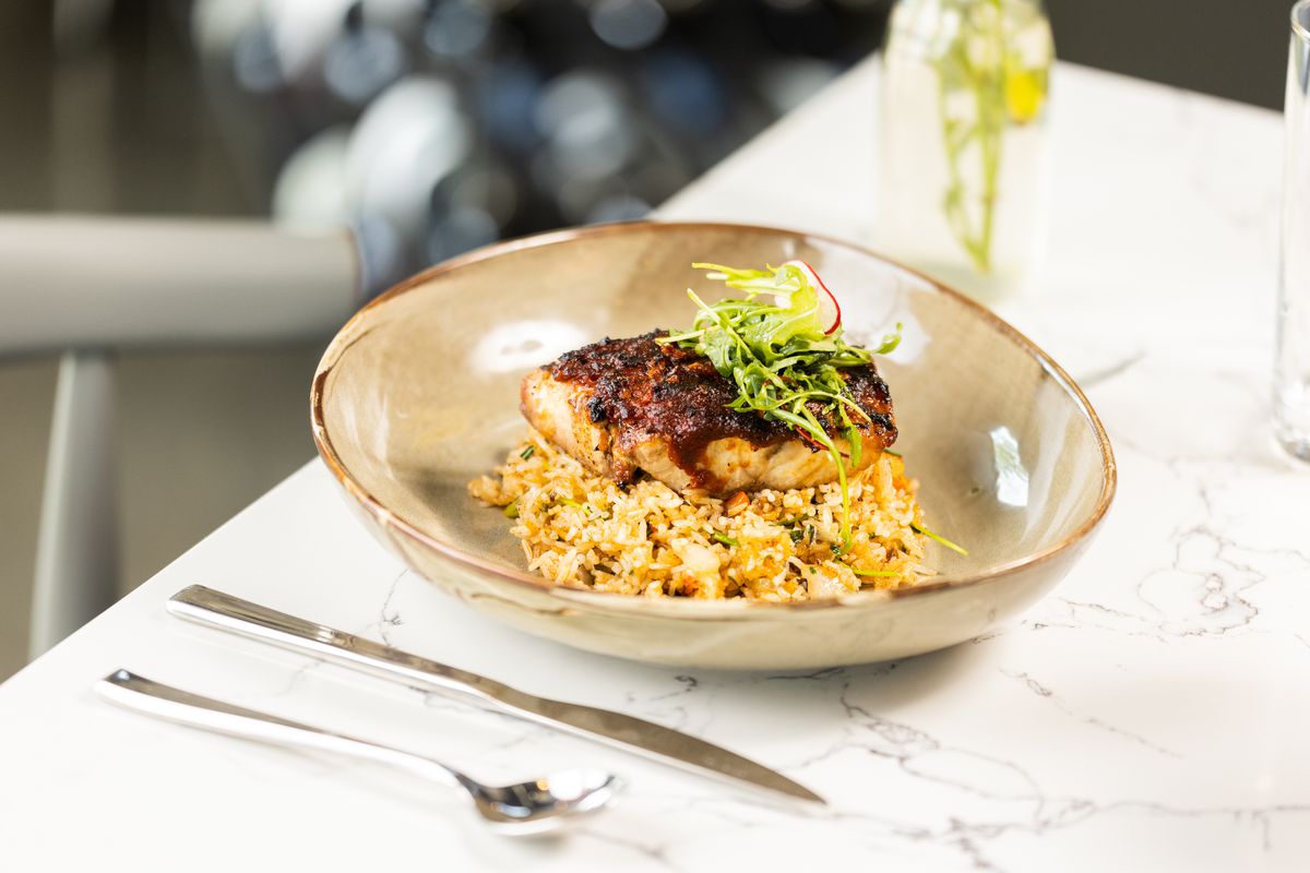 A plate of Texas redfish with harissa sauce sits on top of crawfish fried rice.