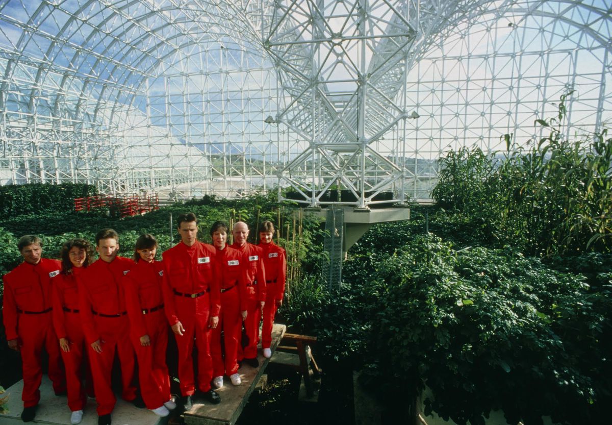 A group of people in red jumpsuits in a glass dome.