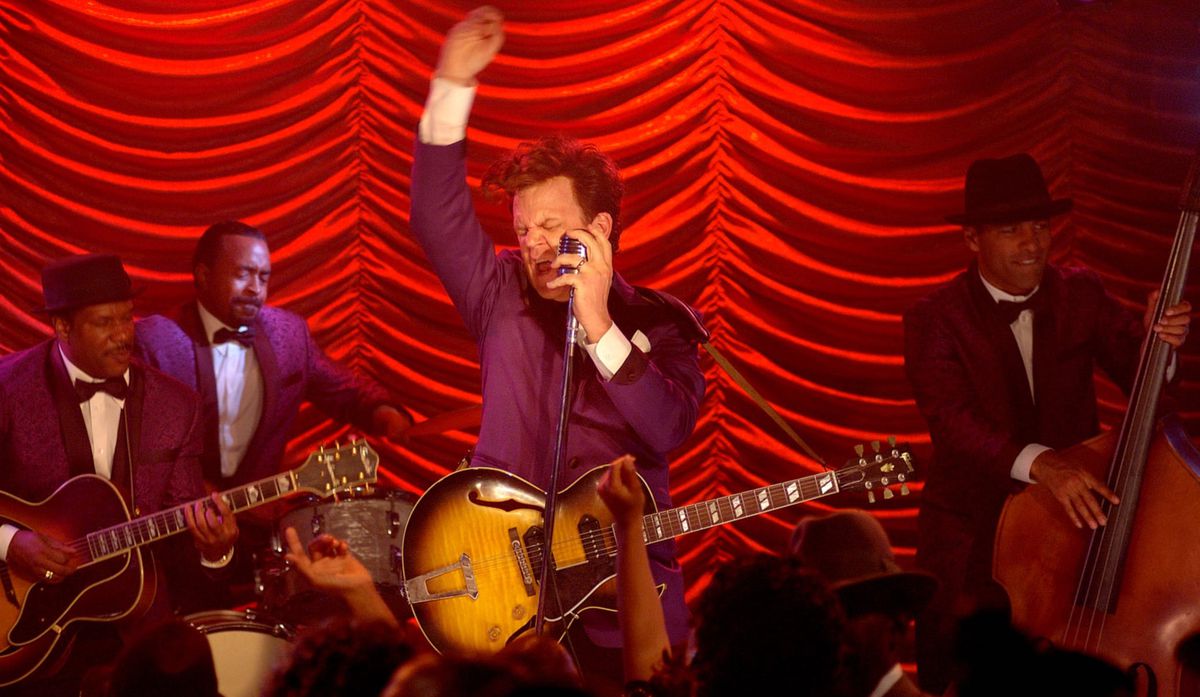 John C. Reilly performs in front of a red curtain and a backing band in Walk Hard