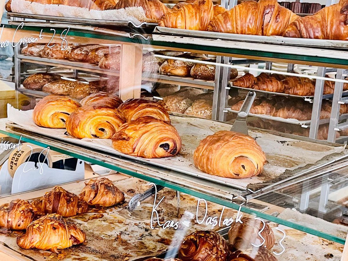 Trays of croissants and other pastries on display in a case with prices written on the glass.