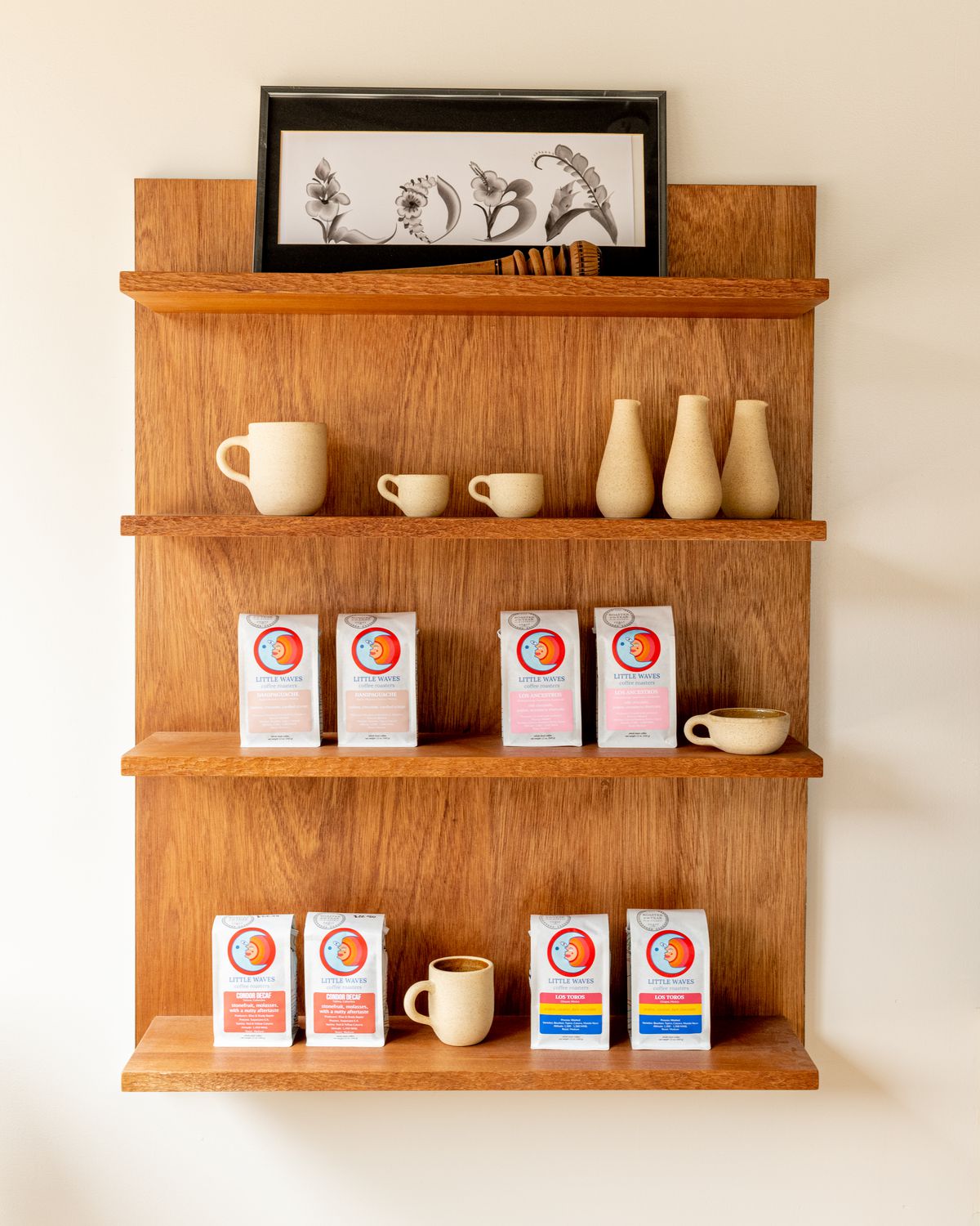 A wooden shelf unit holds bags of coffee beans and earthenware pottery.