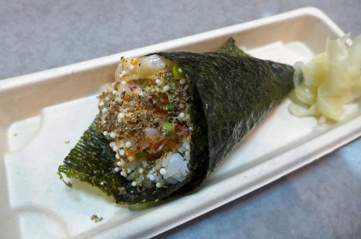 A cone wrapped in nori with black dotted fish spilling out the end.