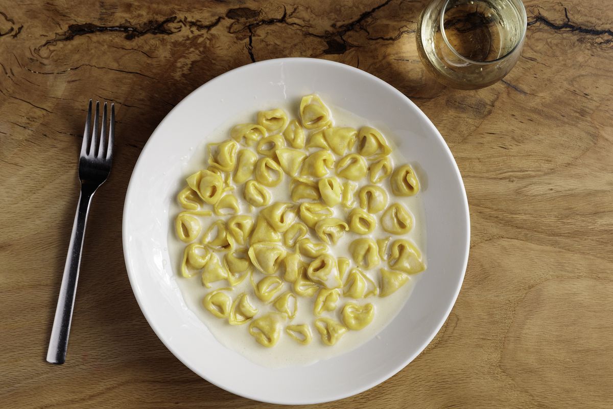Bowl of tortellini in a white cream sauce on a wooden table.
