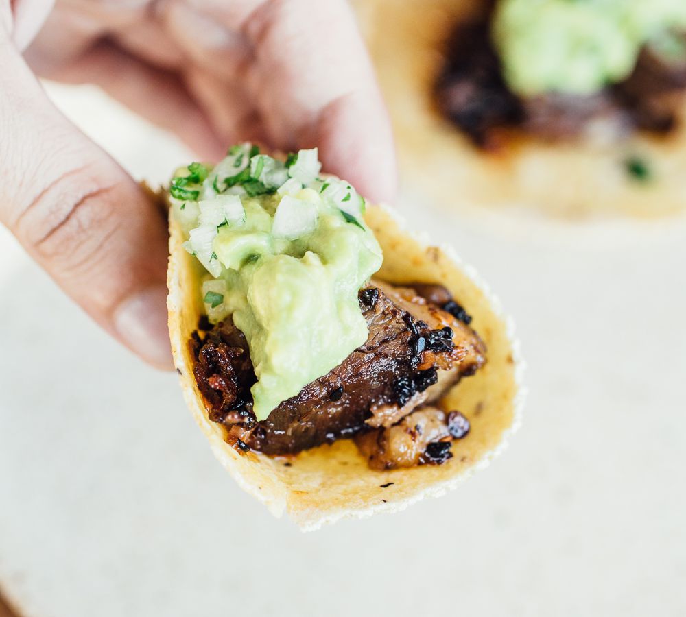 A hand holding up a taco with meat and green sauce.