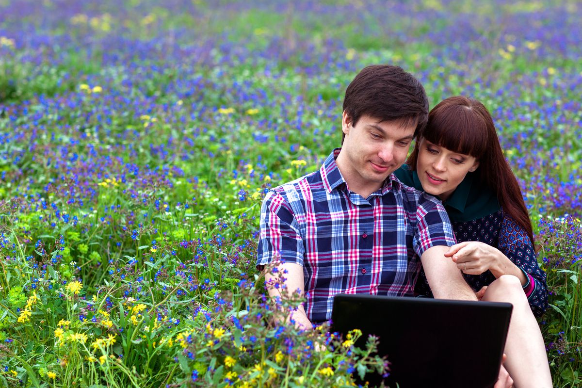 A couple enjoys a moment in a field of flowers, tracking things on a laptop. 