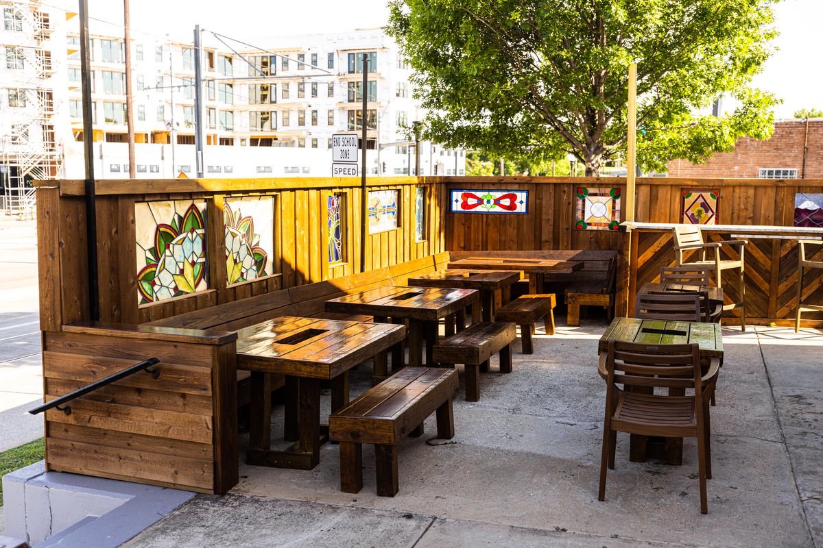 The patio is covered with handmade wooden picnic-style tables, varnished a medium brown. Behind the seats, just above head level, are inserts of stained glass.