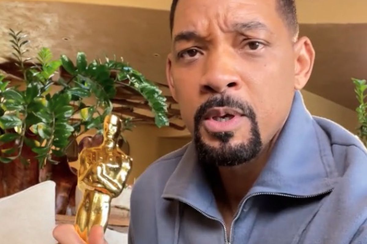 Will Smith holding his oscar statue looking at camera like “huh?” in a nice yellow room with green plants and a white couch