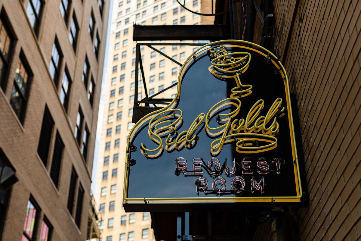 The piano-shaped sign at Sid Gold’s when it’s still light out. It’s built with neon yellow curvy writing with a cocktail coup glass