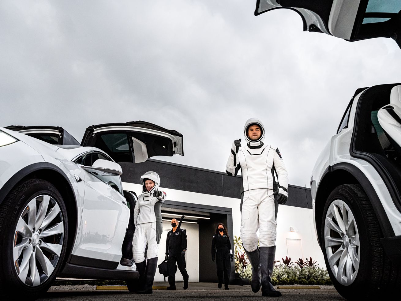 People in astronaut suits exit cars with gull-wing doors.