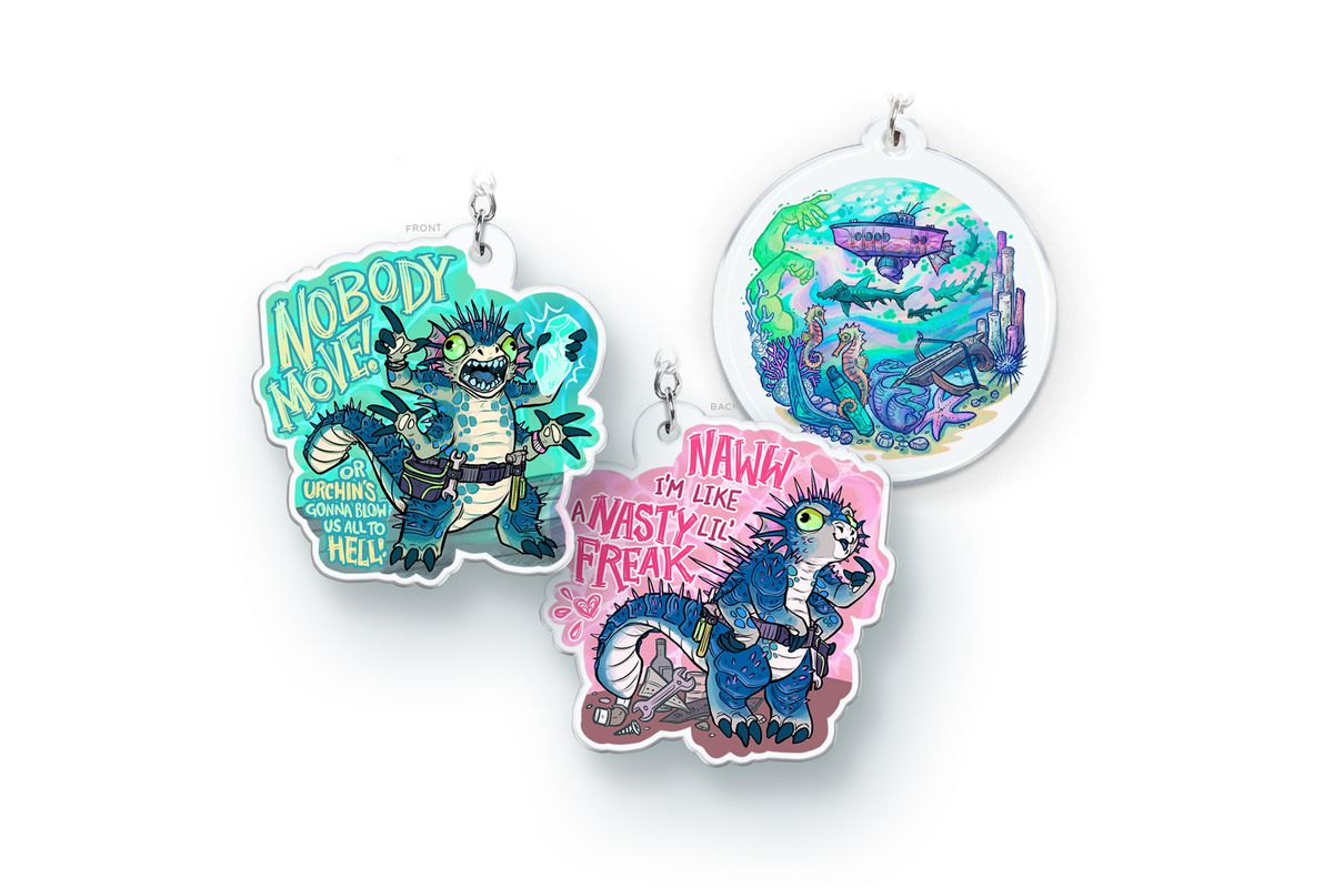 The May McElroy merch items are two keychains: the left and center images are the front and back of an Urchin keychain and the rightmost keychain depicts the Coriolis cruising through the sea. On the left is the front of the keychain. Urchin is holding a crystal. Next to him it says, “Nobody move! Or Urchin’s gonna blow us all to hell!” In the center is the back of the keychain. Urchin is pointing to himself shyly and saying, “Naww I’m like a nasty lil’ freak”.&nbsp;  
