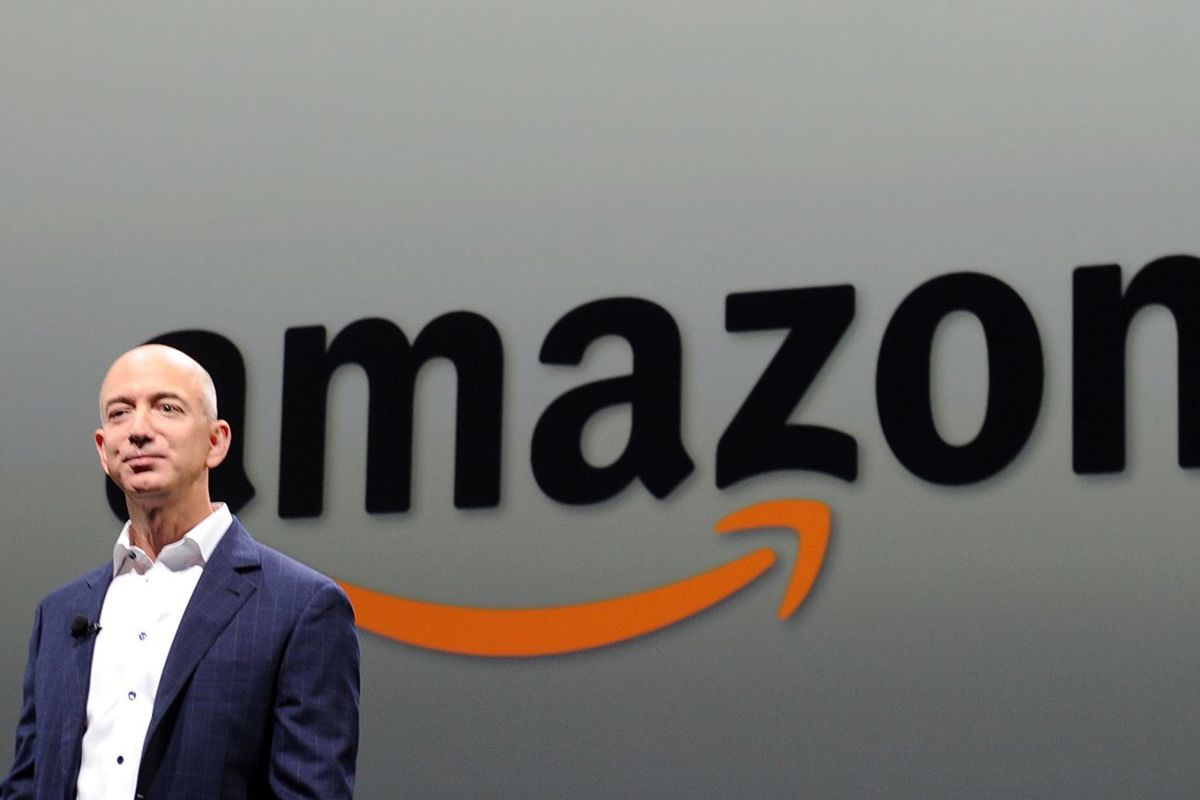 Amazon CEO Jeff Bezos standing in front of the Amazon smiling sign