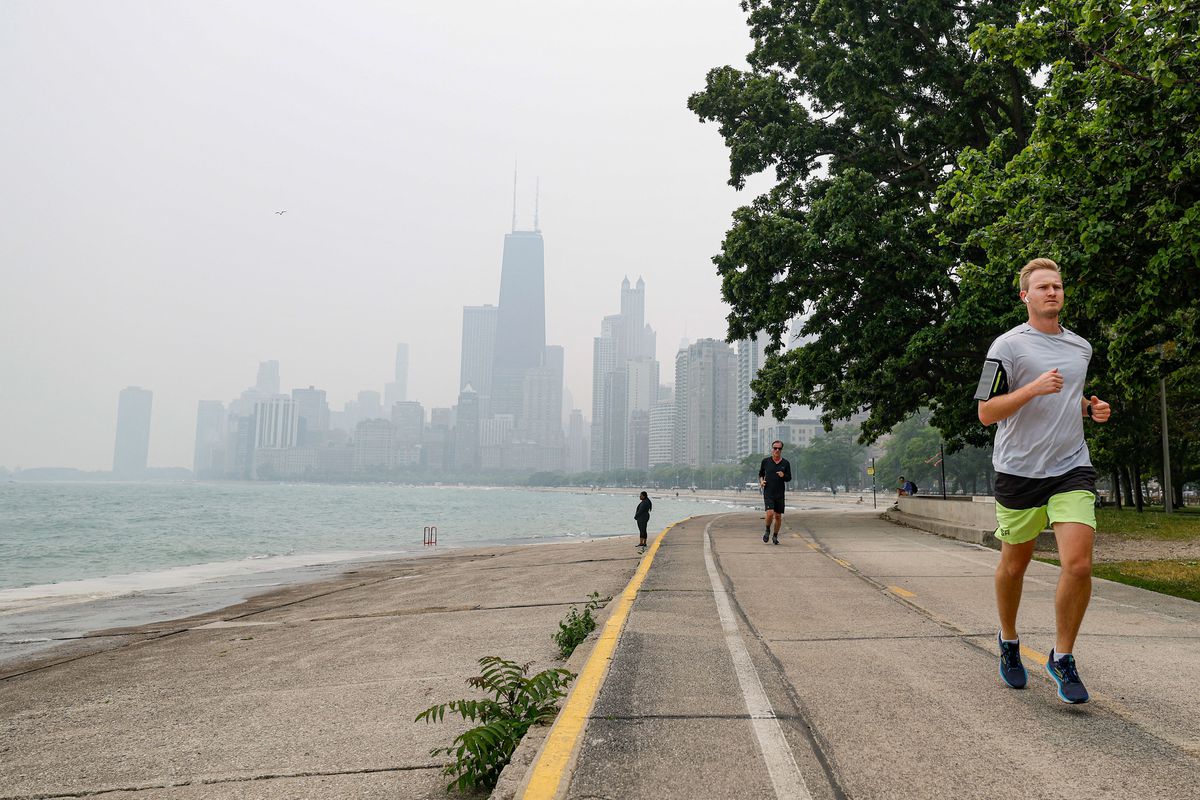 A jogger beside a lake with a smoke-blurred skyline in the background.