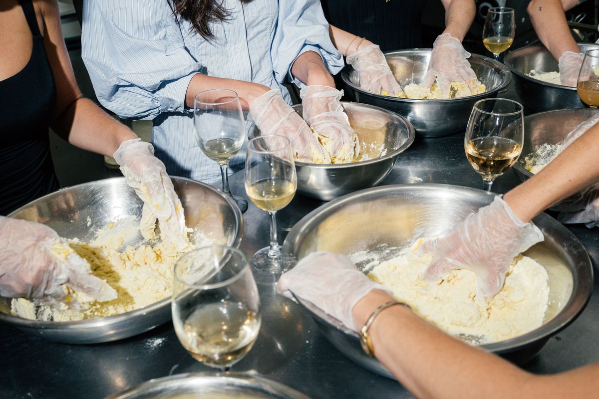 Hands mix the dough next to wine glasses.