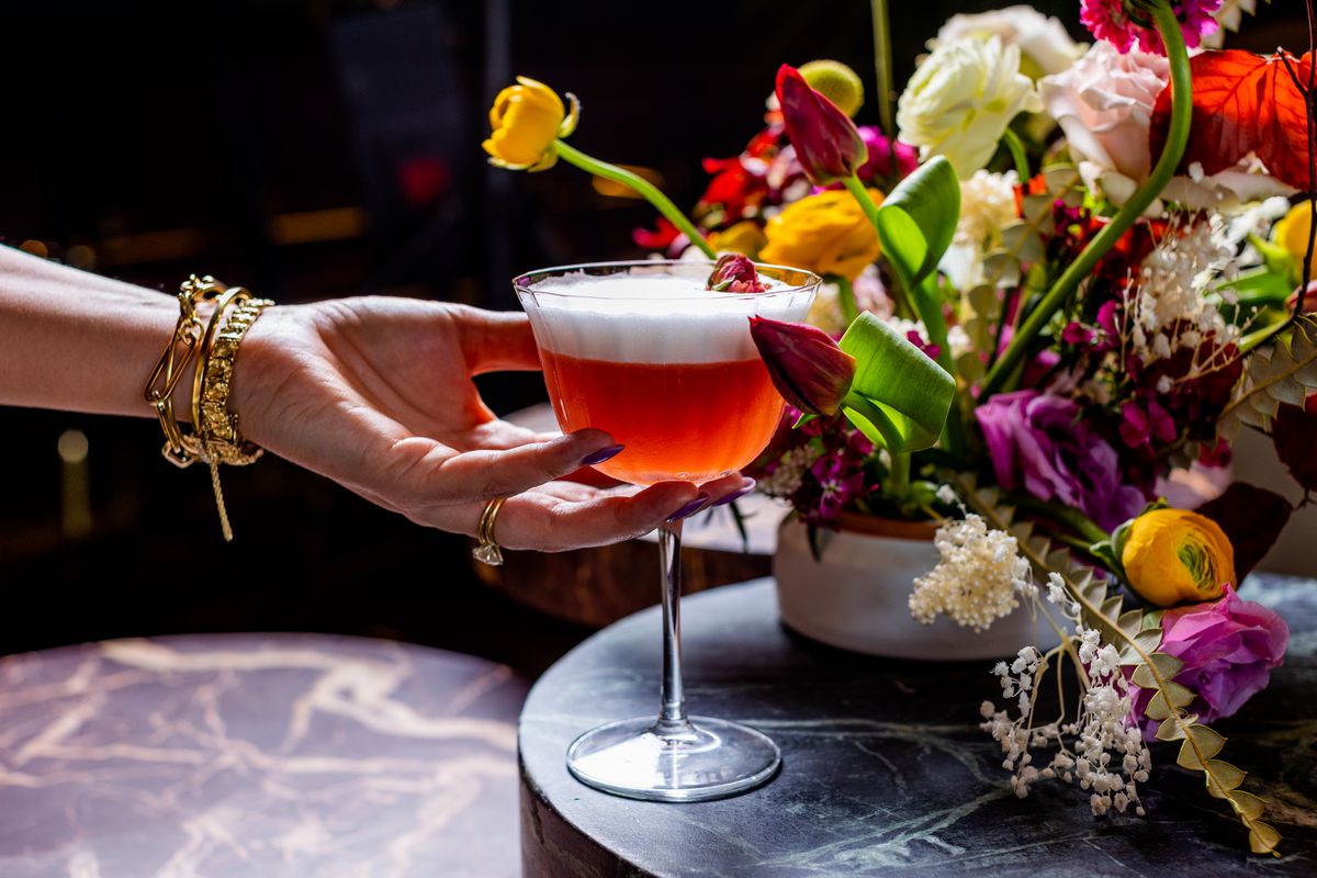 A pretty cocktail next to a floral arrangement. 