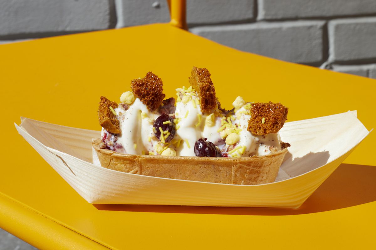 An ice cream sundae in a paper boat, on a yellow table.