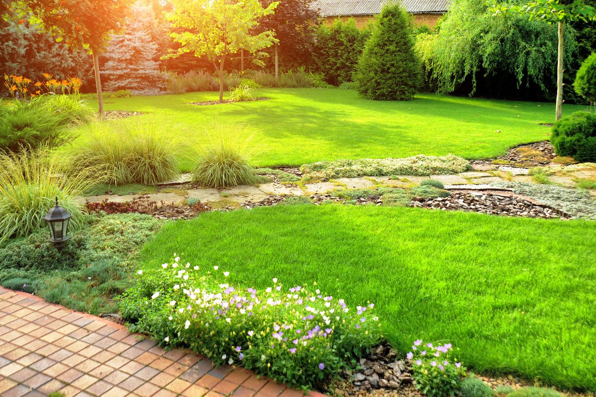 A beautiful, well manicured green grass lawn, with flowers, plants, and a brick pathway