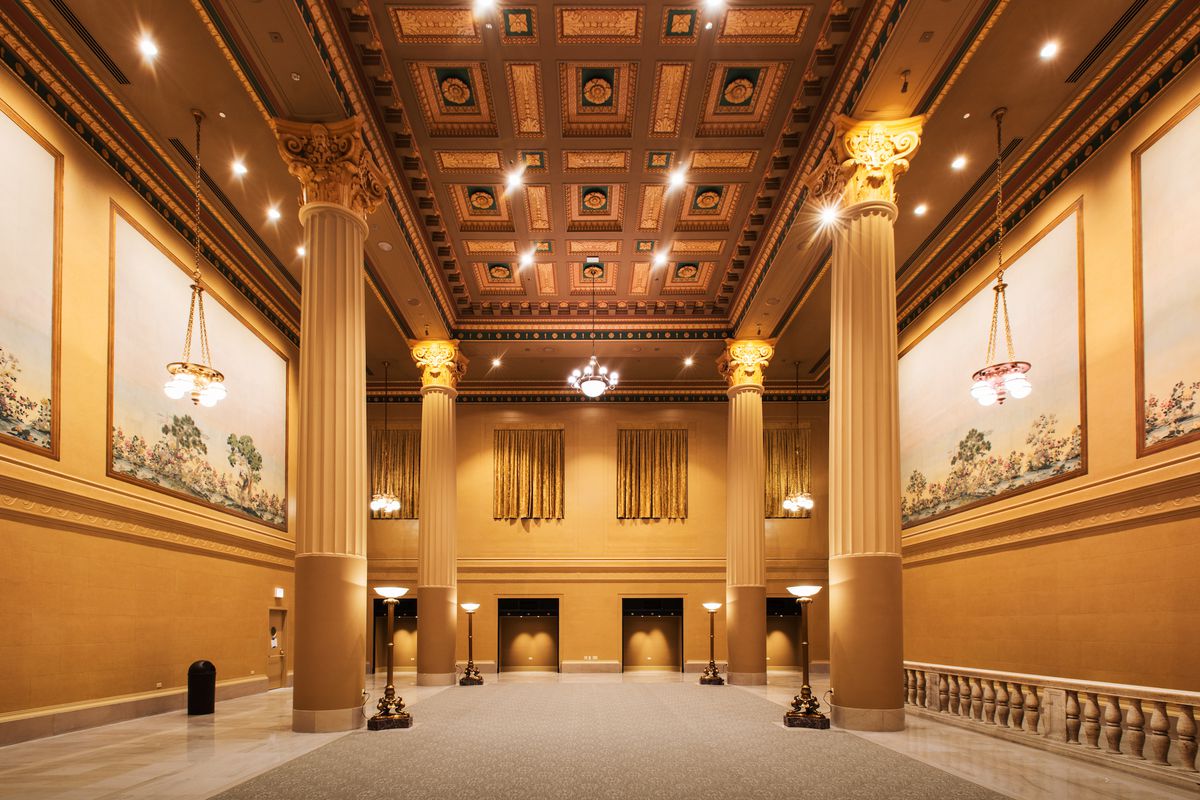 The interior of an event venue. The walls are yellow and the ceiling is wooden with a carved design. There are columns. 
