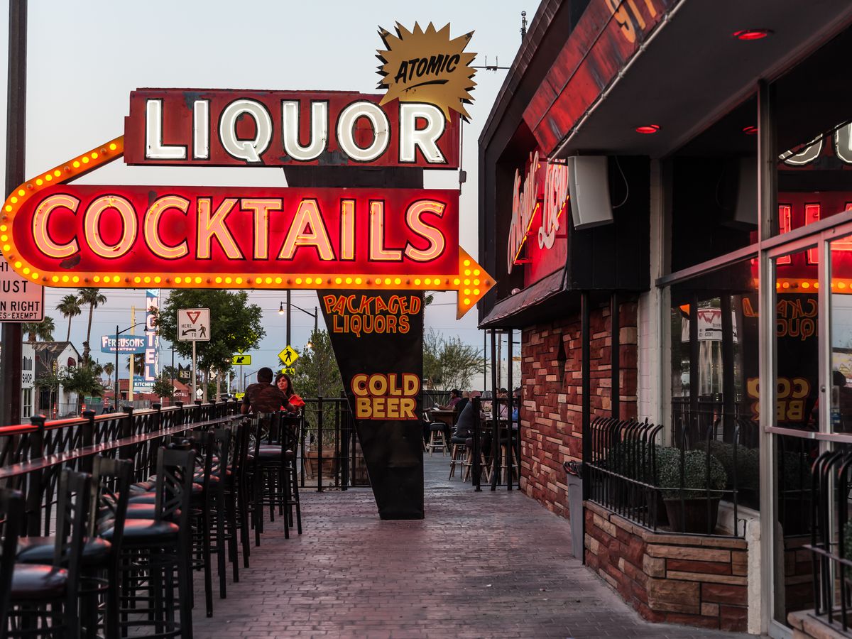 An outdoor patio with a neon sign that says Liquor, Cocktails