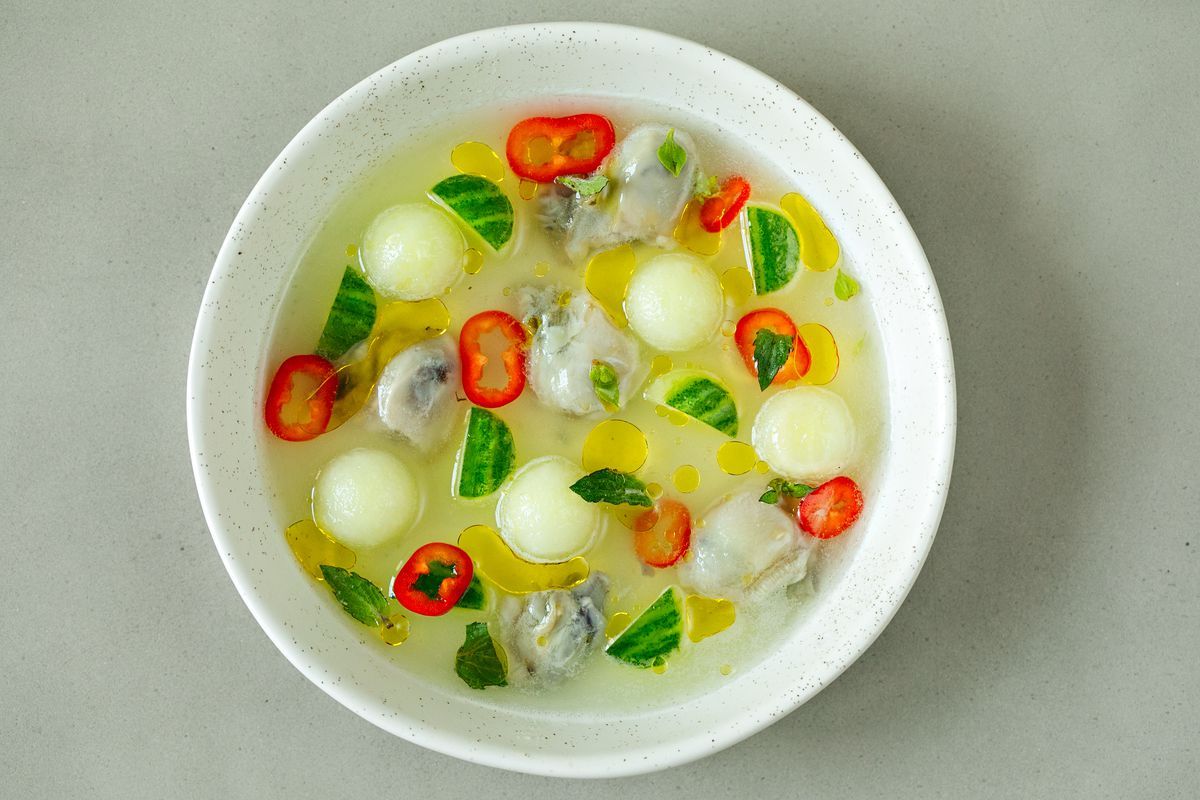 Oyster crudo with melon, cucumber, fennel, and mint on a white plate. 