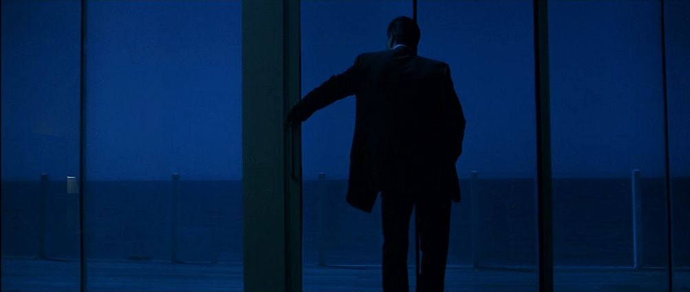 The silhouette of a man (Robert De Niro) leaning against a glass window overlooking an ocean at night in Heat.