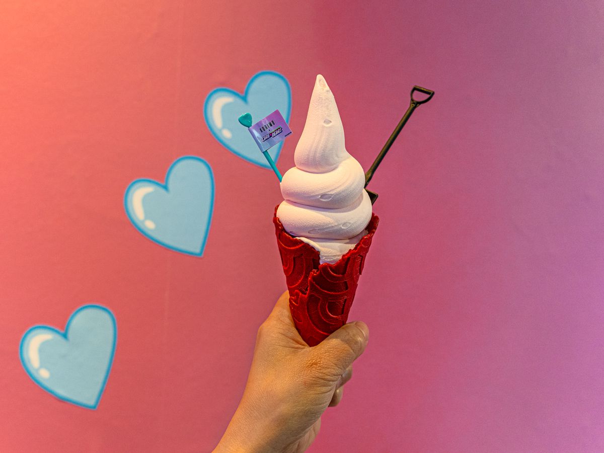A hand holds up a pink ice cream cone.