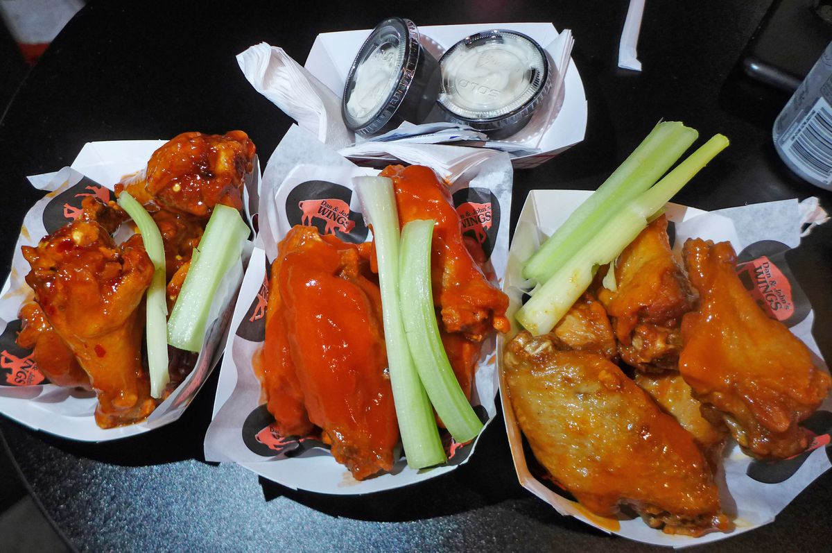 Three paper trays of five wings each, with celery and two white dipping sauces.