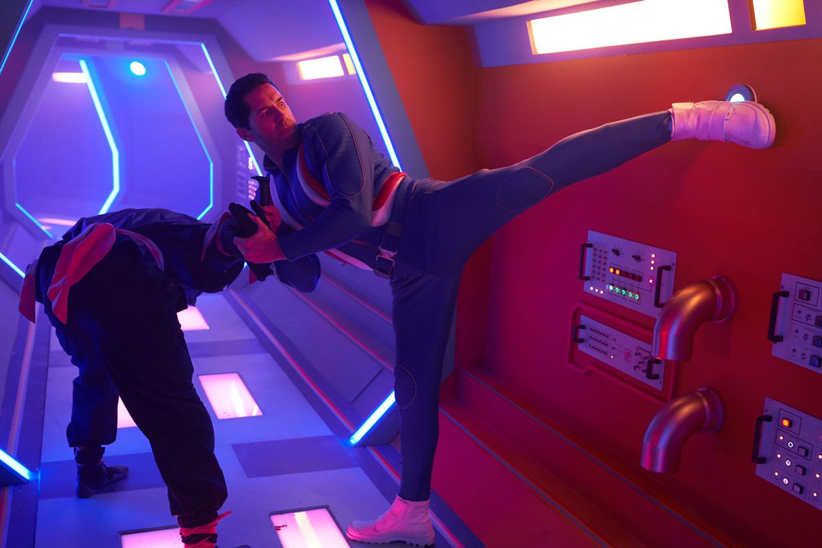 Scott Adkins, in a blue jumpsuit, disables an enemy while kick-activating a button on the wall in Max Cloud