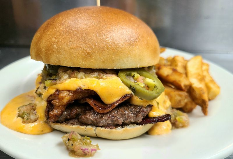 A burger overflowing with cheese, jalapeno, and bacon on a plate with thick-cut fries