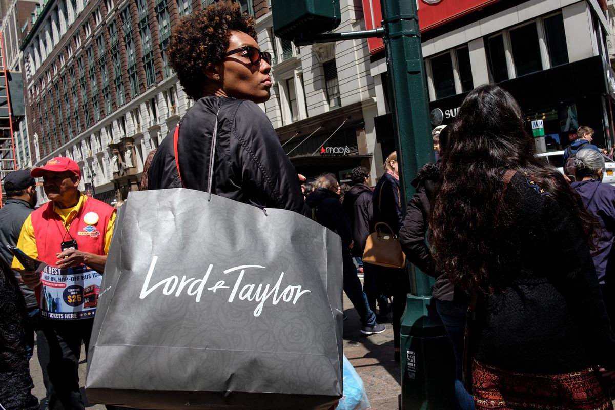 A woman out shopping on a crowded New York street carrying a Lord &amp; Taylor shopping bag