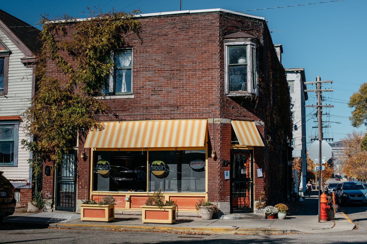 The exterior of the brick, vine-covered building where Mudgie’s is located has orange and white striped awnings.