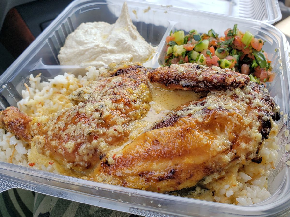 A clear plastic container featuring lemon-garlic chicken, fluffy rice, hummus, and Arabic cucumber-tomato salad at Jerusalem Chicken in View Park-Windsor Hills.