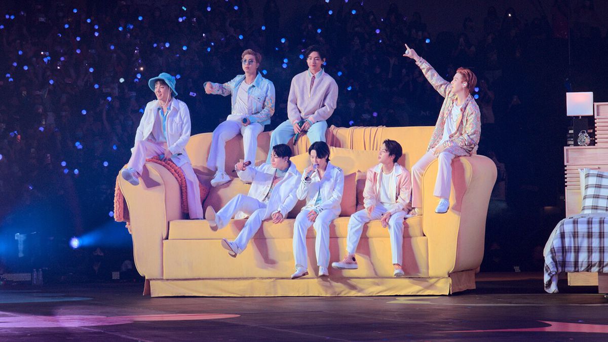 The members of BTS lounge on an oversized couch on stage at their Permission to Dance on Stage LA concert movie.
