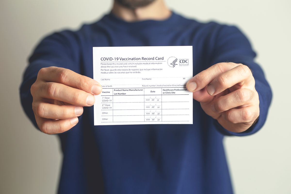 A man holds up a COVID vaccination card