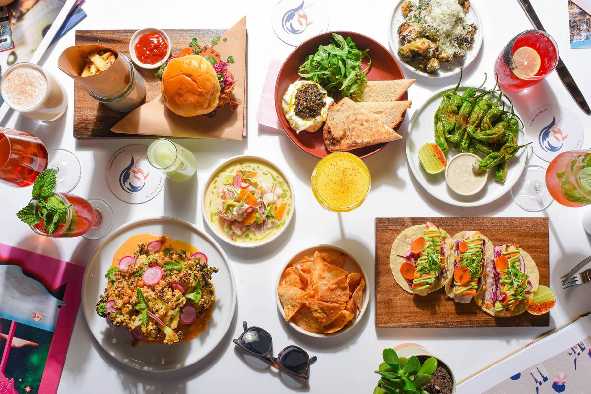 A full spread of sandwiches, plates, tacos, and drinks at daytime against a white table at the new restaurant the Surfing Fox in Santa Monica.