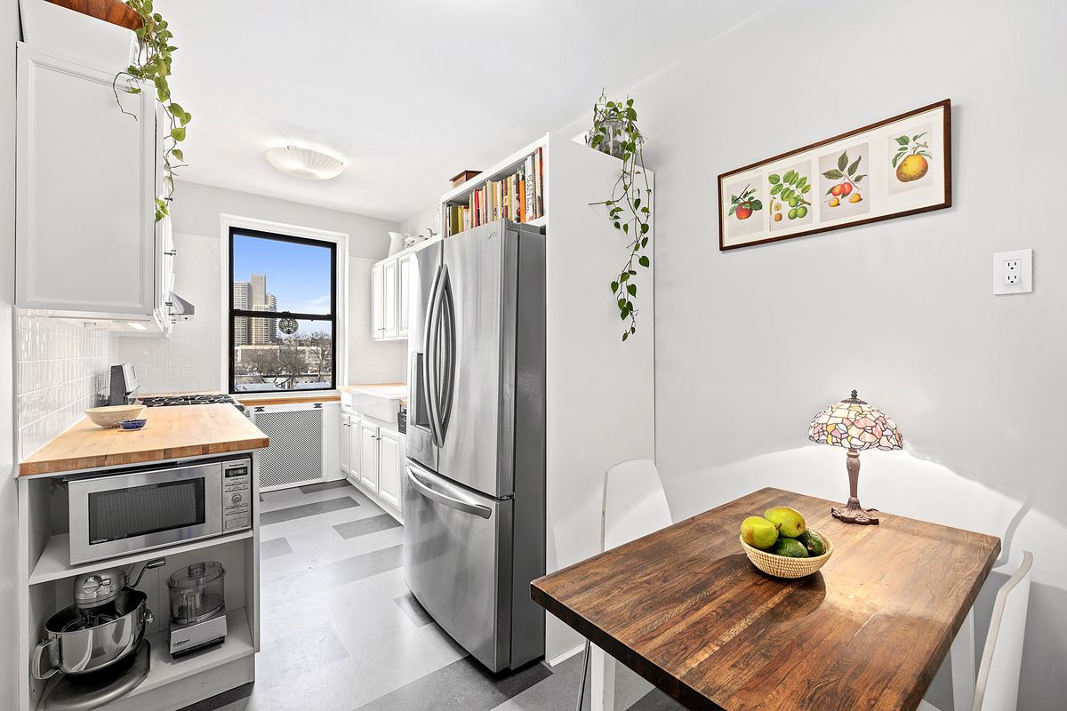 A small kitchen with light grey walls, one window, several planters, and a wooden table.